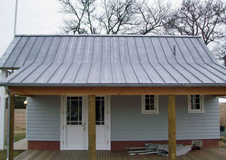 A small house featuring a distinctive metal roof, set against a clear sky.